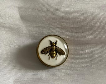 White enamel button featuring an antique gold-tone bee design.