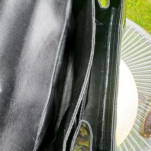 May include: A black leather handbag with a smooth interior lining and multiple compartments. The bag features a structured design with visible stitching along the edges and a deep main opening, showcasing the interior construction and texture.