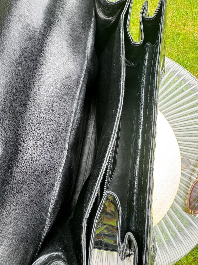 May include: A black leather handbag with a smooth interior lining and multiple compartments. The bag features a structured design with visible stitching along the edges and a deep main opening, showcasing the interior construction and texture.