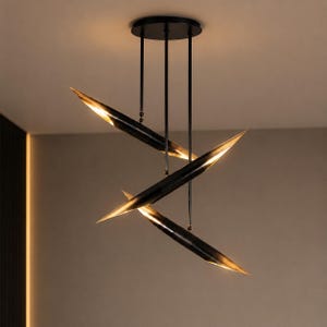 May include: Modern black and gold pendant light fixture. The fixture features three sleek, angled, blade-like elements suspended from the ceiling. Each element has a black exterior and a warm gold interior, creating a striking contrast. The light is designed for a contemporary interior.