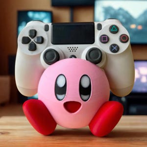 Puede incluir: Una figura rosa del personaje Kirby sosteniendo un mando blanco de PlayStation 4. La figura tiene pies rojos y ojos negros. El mando tiene botones negros y un panel direccional, y botones de acción de colores.