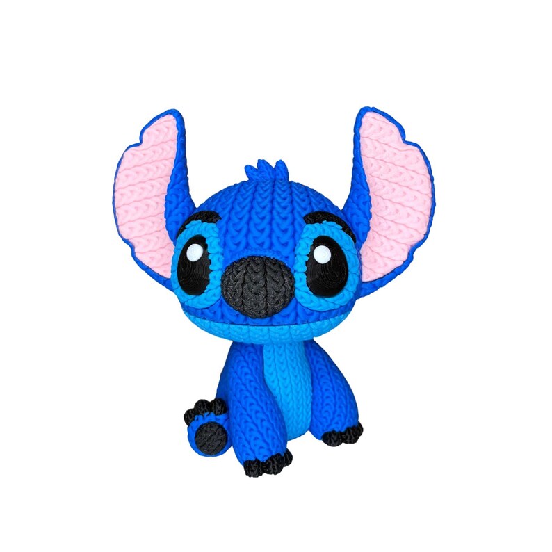 May include: A blue knitted Stitch figurine with large black eyes, a black nose, and pink inner ears. The figurine is sitting with its arms and legs outstretched. The Stitch character is from the Disney movie Lilo & Stitch.