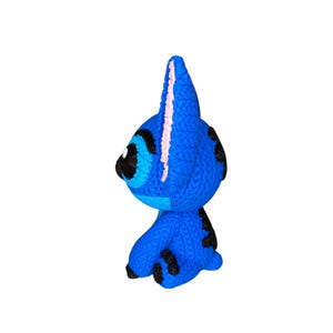 May include: A blue knitted character with black spots and a pink stripe down the head. The character has large black eyes and is in a sitting position. The toy is a handmade item.