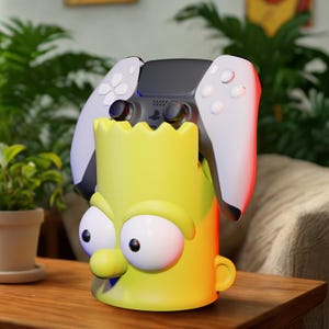 Puede incluir: Un soporte amarillo para mando con el tema de Bart Simpson con un mando de PlayStation 5. El soporte tiene un diseño de dibujos animados con ojos grandes y una expresión traviesa. El mando es blanco y negro.