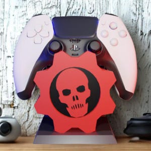 Può includere: Un supporto per controller di gioco rosso e nero con un design a teschio all'interno di una forma di ingranaggio. Contiene un controller di gioco bianco e nero. Il design è probabilmente ispirato alla serie di videogiochi Gears of War.