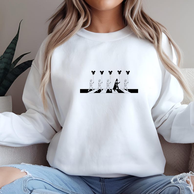 May include: White sweatshirt featuring a black and white graphic of characters crossing a crosswalk, each holding a Mickey Mouse-shaped balloon. The design is a parody of the iconic Abbey Road album cover.