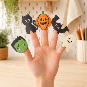 May include: A set of five Halloween-themed finger puppets made of paper. The characters include a green Frankenstein monster, a black cat, an orange jack-o'-lantern, a black bat, and a cream-colored ghost, each featuring googly eyes.