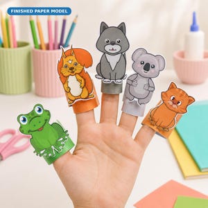 Könnte beinhalten: Ein Set aus fünf Fingerpuppen aus Papier, bestehend aus einem grünen Frosch, einem orangefarbenen Eichhörnchen, einem grauen Wolf, einem grauen Koala und einer orangefarbenen getigerten Katze. Jedes Tier ist auf einer zylindrischen Papierbasis befestigt.