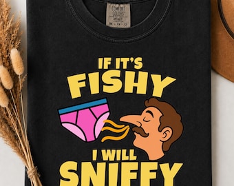 May include: A black t-shirt featuring a graphic of a person with brown hair and a mustache sniffing a pair of pink underwear with a blue waistband. The text reads IF IT'S FISHY I WILL SNIFFY in yellow letters. The shirt has a Comfort Colors brand label.