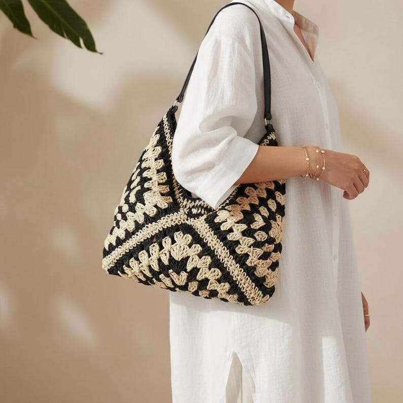 May include: A black and beige crochet tote bag with a geometric pattern. The bag has black leather straps and is carried over the shoulder. The bag is made of a woven material and has a structured shape.