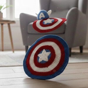 K&ouml;nnte beinhalten: Geh&auml;kelte Artikel im Captain America-Design. Das Bild zeigt einen Schild und einen Hut, beide in Rot, Wei&szlig; und Blau. Der Schild hat einen wei&szlig;en Stern, und der Hut hat ein wei&szlig;es "A" und Fl&uuml;gel. Diese handgefertigten Artikel sind f&uuml;r Kinder geeignet.