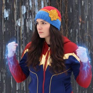May include: A red, blue, and yellow knit hat with a star-shaped embellishment. The hat is worn with a blue and red zip-up jacket with gold accents. The jacket has a star design on the chest.
