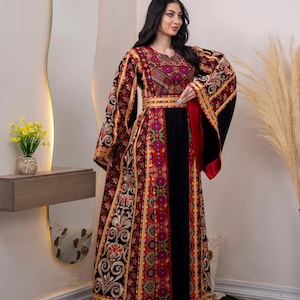 May include: A long, embroidered dress with a black bodice and sleeves. The dress features intricate patterns in red, gold, and purple. The sleeves are wide and flowing, and the dress has a fitted waist. The dress is a traditional garment.