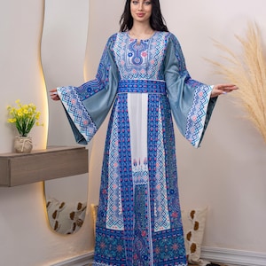 May include: A long, flowing dress with a blue and white geometric pattern. The dress features wide sleeves, a cinched waist, and intricate embroidery around the neckline and hem. The dress is worn by a person with long, dark hair.