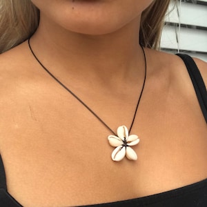 May include: A black cord necklace with a white seashell flower pendant.