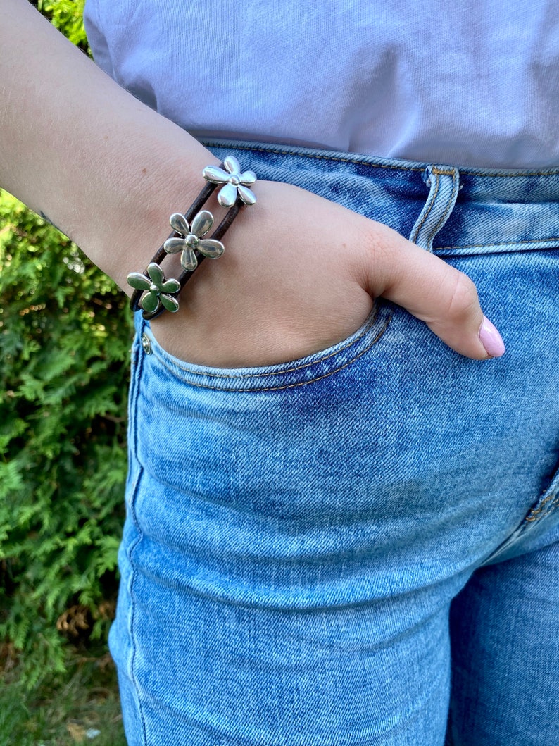 May include: A brown leather bracelet with three silver flower charms.