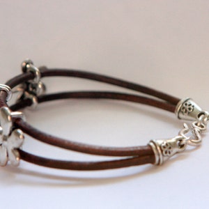 May include: A brown leather bracelet with silver flower charms and a silver clasp.