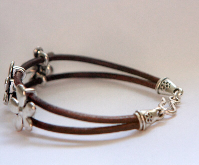 May include: A brown leather bracelet with silver flower charms and a silver clasp.
