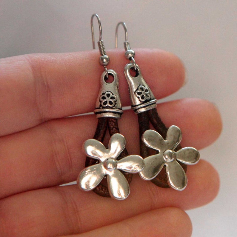 May include: Silver dangle earrings with brown leather cord and flower charms.