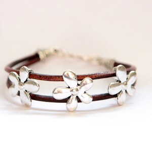 May include: A brown leather bracelet with three silver flower charms.