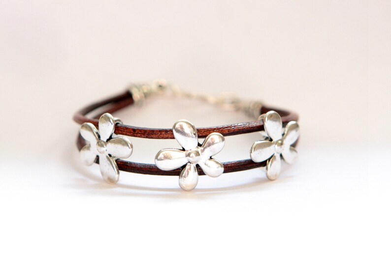 May include: A brown leather bracelet with three silver flower charms.