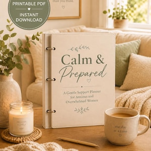 May include: A cream-colored ring-bound planner with the text Calm & Prepared A Gentle Support Planner for Anxious and Overwhelmed Women, a candle labeled BREATHE SLOWLY, a mug with the text one day at a time, and a gold pen on a wooden surface.