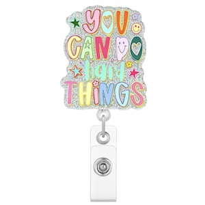 May include: A badge reel featuring a silver glitter background with the colourful text YOU CAN DO HARD THINGS. The design includes small icons of stars, a smiley face, and flowers in shades of pink, yellow, blue, and green. A white plastic clip is attached.
