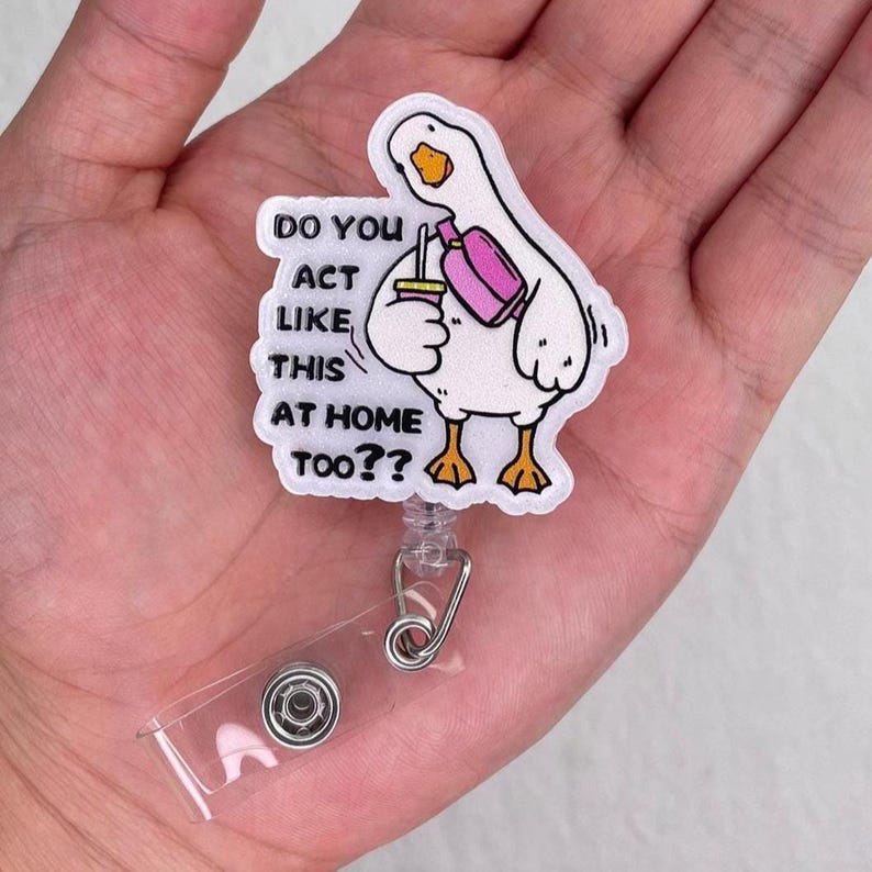 K&ouml;nnte beinhalten: Ein wei&szlig;es G&auml;nse-Cartoon-Ausweis-Jojo mit dem Text "DO YOU ACT LIKE THIS AT HOME TOO??". Die Gans h&auml;lt ein Getr&auml;nk und eine rosa Tasche. Das Ausweis-Jojo hat einen transparenten Kunststoffriemen und einen Metallclip.