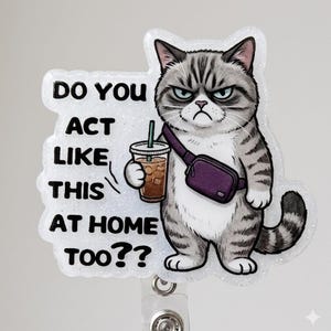 May include: A glittery badge reel featuring a grumpy grey tabby cat wearing a purple crossbody bag and holding an iced coffee. The text reads, DO YOU ACT LIKE THIS AT HOME TOO?? The design is printed on a clear, shimmering, die-cut acrylic shape.