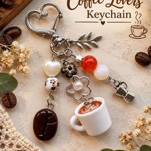 May include: A silver-toned keychain featuring a heart-shaped clasp, a leaf charm, and three dangling strands. The strands include a dark brown coffee bean bead, a white coffee cup charm with latte art, and a miniature silver moka pot.