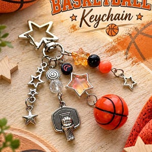 May include: A silver-toned keychain featuring a star-shaped clasp, multiple dangling charms including a basketball hoop, a miniature orange basketball, various star charms, and beads in orange, black, and clear with a crescent moon symbol.
