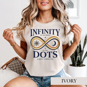 May include: An ivory short-sleeve t-shirt featuring a graphic with the text INFINITY NO BEGINNING NO END DOTS ALWAYS CONNECTED. The design includes a large infinity symbol in shades of gold, brown, and blue, containing a compass and moon.