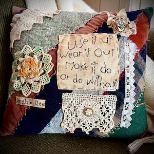 May include: A patchwork pillow with various fabric textures and colors, including green, blue, and red. The pillow features lace and crocheted embellishments, with the text "Use it up Wear it Out Make it do or do Without" embroidered on a fabric patch. The words "Laugh • live" are also visible.