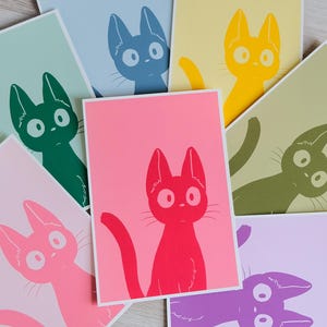 Peut inclure: Plusieurs impressions d'art colorées avec des illustrations de chats stylisés. Chaque impression présente un chat de couleur différente, notamment rose, rouge, jaune, vert, bleu et violet, sur un fond assorti. Les traits du chat sont simplifiés avec de grands yeux et des oreilles pointues.