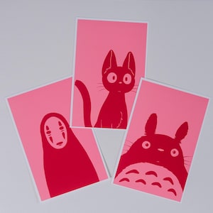Peut inclure: Trois affiches roses avec des illustrations rouges de personnages. L'une représente un chat, une autre un personnage masqué et la troisième une créature ronde avec de grandes oreilles. Chaque affiche a un bord blanc.