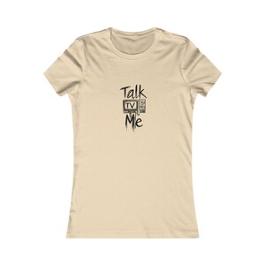 May include: A light beige fitted t-shirt with the text "Talk TV Me" in black. The graphic includes a vintage television and speaker design. The shirt is made of a soft material and has a crew neck.