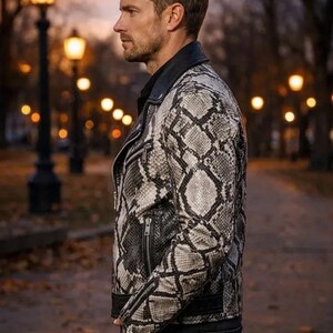 May include: A snakeskin-patterned leather jacket in shades of gray and black. The jacket features a classic biker style with a notched collar, zippered pockets, and a fitted silhouette. The model is wearing black jeans.
