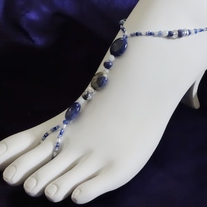 Pode incluir: Uma joia de pé azul e branca com uma pulseira de tornozelo e um anel de dedo do pé. A joia apresenta pedras azuis e brancas.