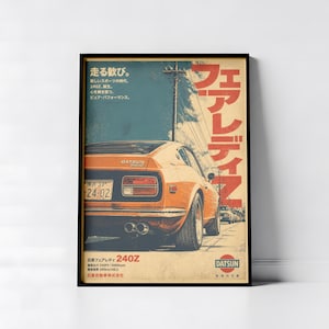 May include: A framed poster featuring an orange Datsun 240Z sports car viewed from the rear. The artwork includes Japanese text, a license plate reading 24-02, dual exhaust pipes, and the Datsun logo. The scene depicts the car on a road with a utility pole under a blue sky.