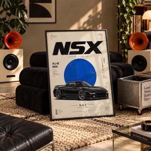 Peut inclure: Une affiche verticale encadrée présentant une illustration de voiture Honda NSX noire centrée sous un grand cercle bleu. Le texte indique NSX, Legends Lives On, NA1 1990-2005, et inclut des caractères japonais. Le design a un fond crème avec des accents noirs.