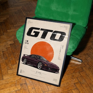 Puede incluir: Un póster enmarcado que muestra un coche deportivo Mitsubishi GTO Z16A de color morado oscuro bajo un gran círculo naranja. El texto incluye GTO, LEGEND LIVES ON, Z16A 1990-2000 y caracteres japoneses. El diseño tiene una estética vintage sobre fondo blanco roto.