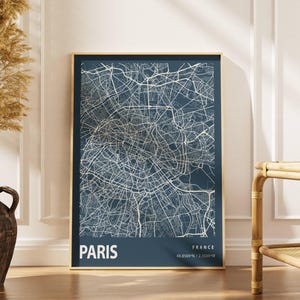 Könnte beinhalten: Eine gerahmte Karte von Paris, Frankreich, in Marineblau und Weiß. Die Karte zeigt das Straßennetz der Stadt. Das Wort "PARIS" ist unten in Weiß gedruckt, zusammen mit den Koordinaten. Der Rahmen ist goldfarben.
