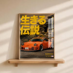 Puede incluir: Un póster enmarcado que muestra un coche deportivo Porsche 911 RWB de color naranja brillante aparcado frente a un edificio japonés tradicional. El póster incluye grandes caracteres japoneses amarillos, el texto RAUH-Welt BEGRIFF y un pequeño icono de bandera japonesa.