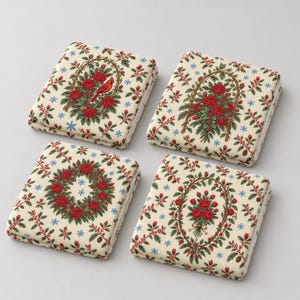 May include: Four square fabric coasters featuring a cream background with a repeating pattern of red roses, green holly leaves, pinecones, and small blue snowflakes. One coaster displays a red cardinal bird perched within a floral arch.