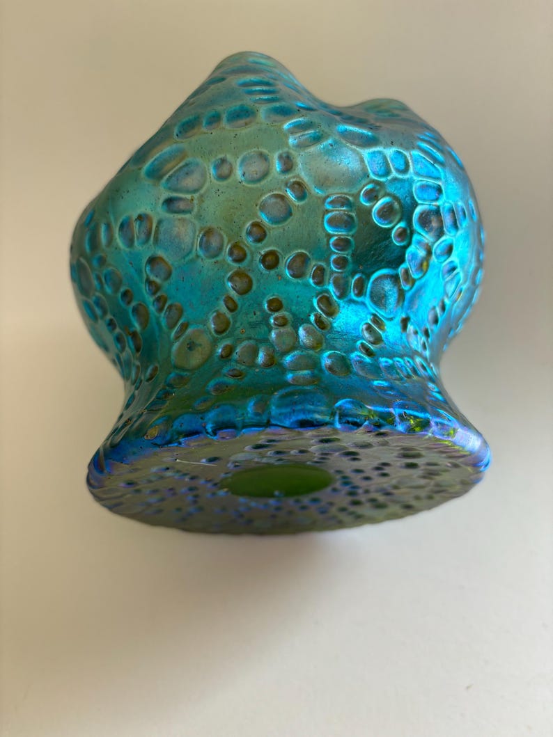 May include: A glass vase with an iridescent finish in shades of teal, blue, and green. The surface features a raised, textured pattern of interconnected circular and organic shapes that create a tactile, honeycomb-like appearance across the body.