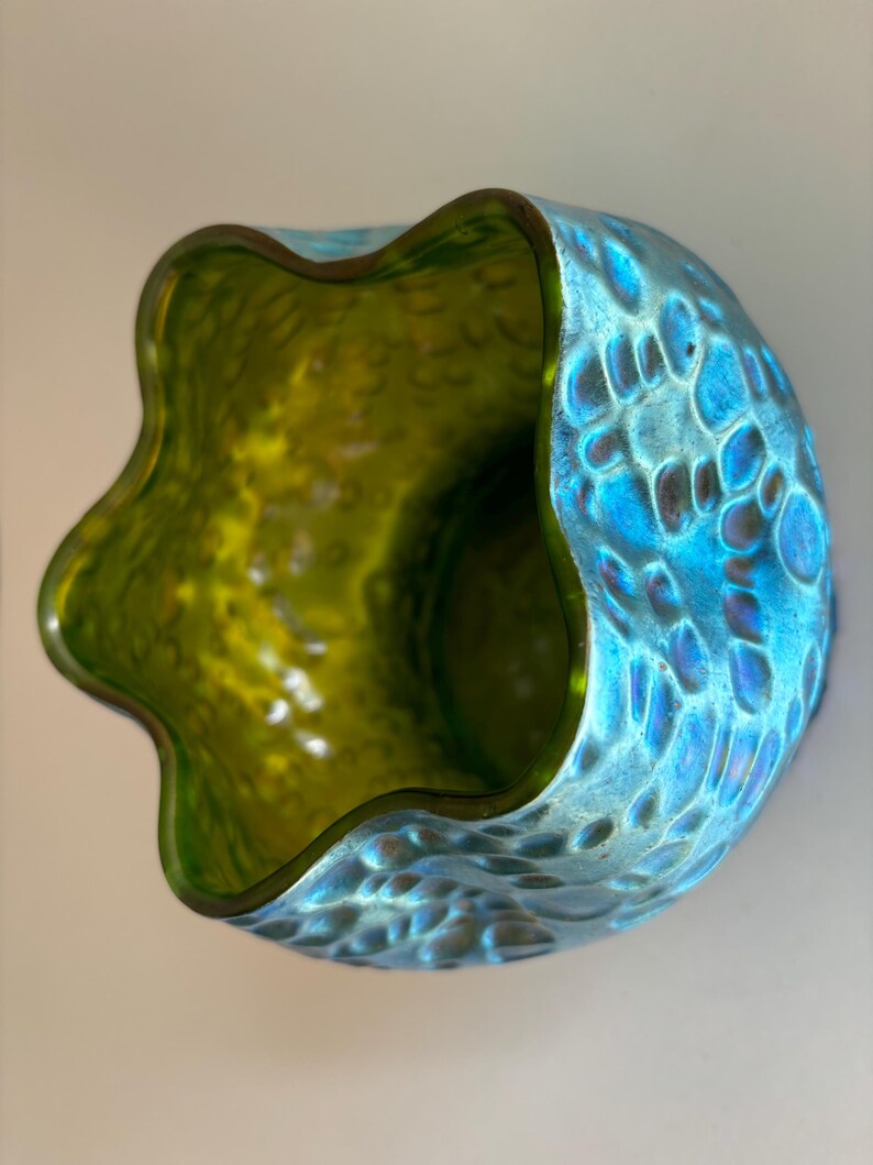 May include: A glass bowl with a wavy, scalloped rim. The exterior features a textured, dimpled surface with an iridescent blue finish, while the interior is a smooth, translucent lime green color. The bowl has a rounded, bulbous shape.