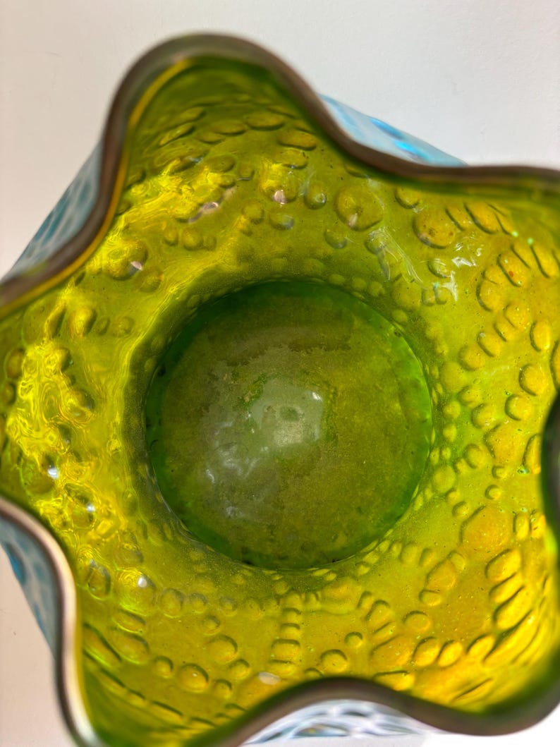 May include: A top-down view of a glass vase featuring a vibrant lime green interior with a textured, bubbled surface. The rim has a wavy, scalloped edge, and the exterior transitions into a bright turquoise blue color with a matching bubbled pattern.