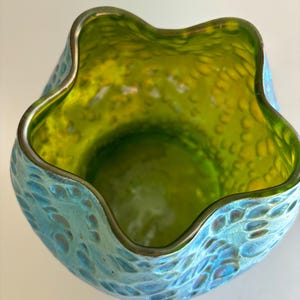 May include: A glass vase with a scalloped, wavy rim. The interior is a vibrant lime green, while the exterior features a textured, iridescent blue finish with a pattern of raised, rounded bumps that catch the light across the surface.