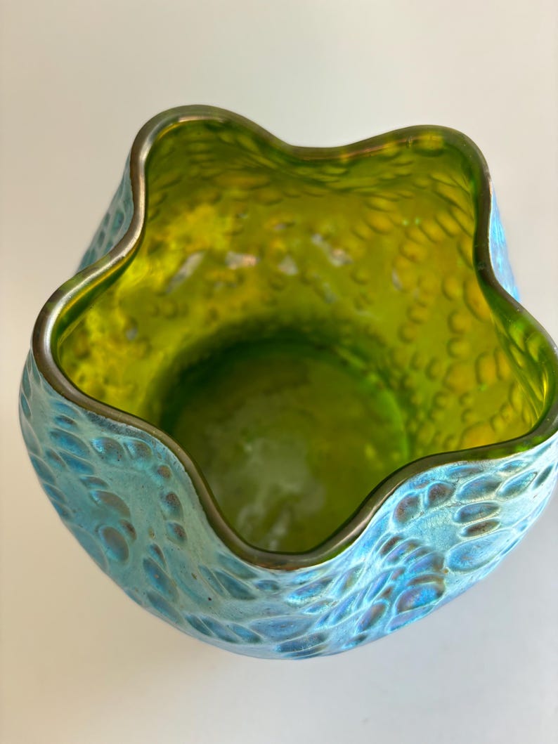 May include: A glass vase with a scalloped, wavy rim. The interior is a vibrant lime green, while the exterior features a textured, iridescent blue finish with a pattern of raised, rounded bumps that catch the light across the surface.