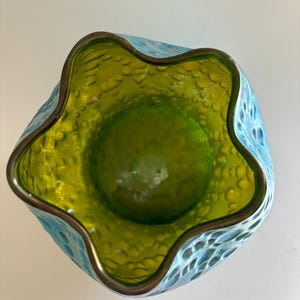 May include: A glass bowl with a wavy, five-pointed star-shaped rim. The interior is a vibrant lime green, while the exterior features a textured, bubbled surface in a bright turquoise blue. The rim is finished with a thin, metallic bronze edge.